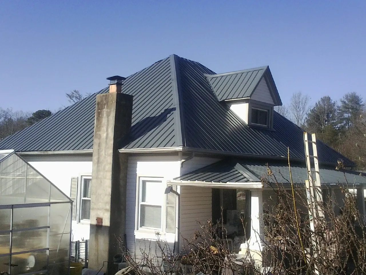 Dark blue standing seam metal roof on a white farmhouse with dormer — Slate & Tile Roof Repair by Roofing Brothers in Butte Falls