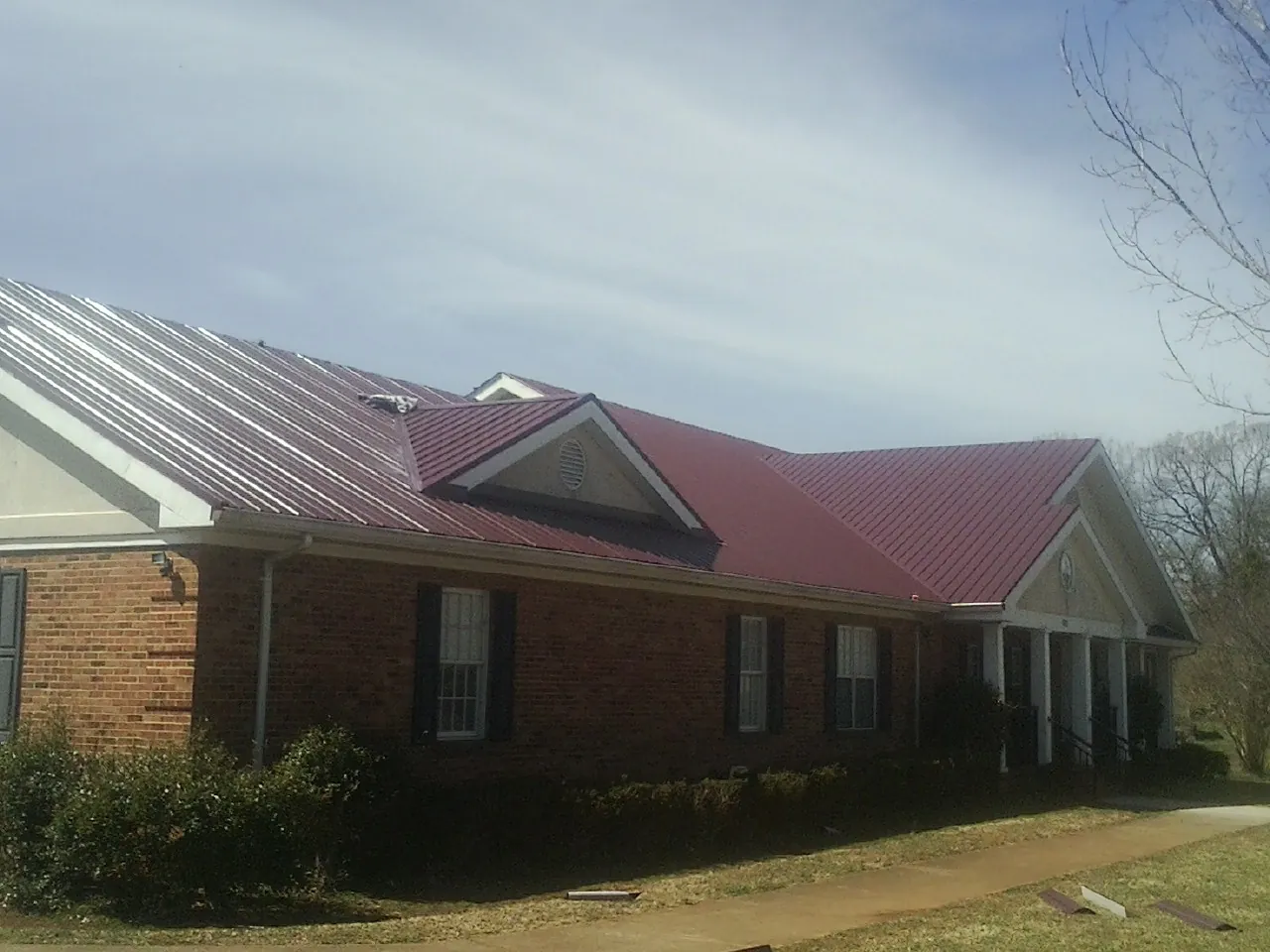 Red metal roof with gabled entries on a long brick building, from a Hail Damage Roof Repair job in Butte Falls