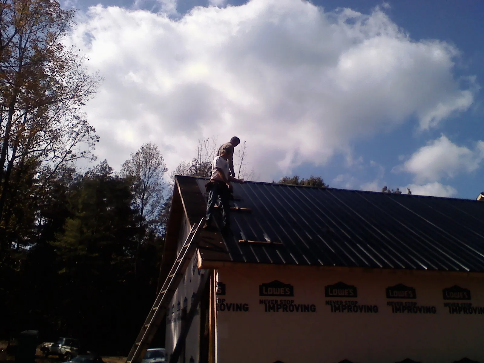 Roofer fastening dark metal panels high against a cloudy sky, from a Roof Inspection job in Butte Falls