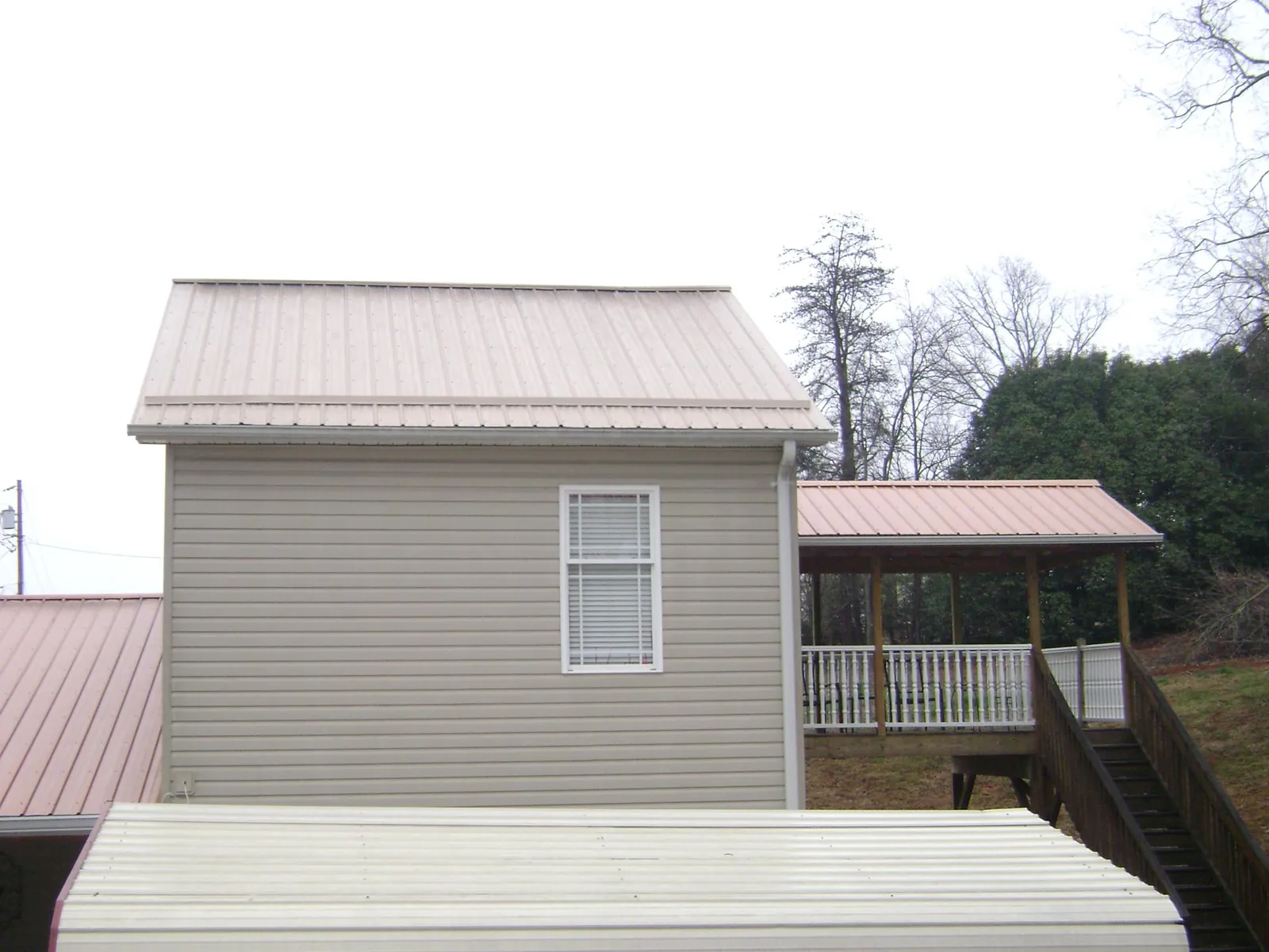 Tan metal roofs on a two story addition and attached porch, from a Roof Replacement job in Butte Falls